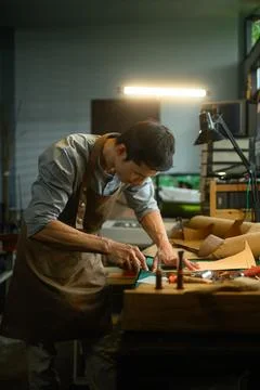 Concentrated artisan carefully using a sharp knife to shape the leather on Stock Photos