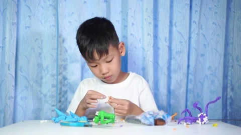 Concentrated Asian boy Sitting and making dolls from plasticine Stock-Footage 219923367