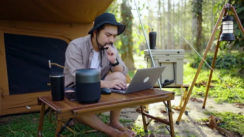 Concentrated Asian man using laptop working remotely while camping in the forest Stock Footage 168486168