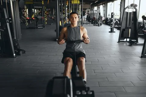 Concentrated athlete guy exercising on a rowing machine in a modern gym Stock Photos