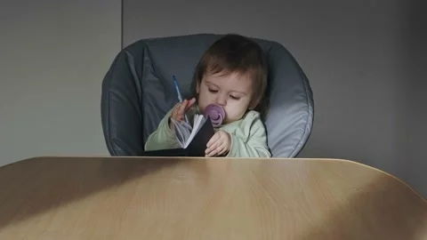 Concentrated baby sitting at the head of the table and flipping through a Stock Footage 194460423