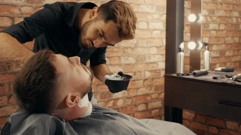 Concentrated barber applying foam on beard Stock Footage 125130699