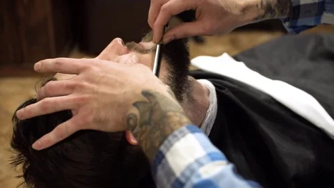 Concentrated Barber shaving beard of client with barber razor Stock Footage 69990005