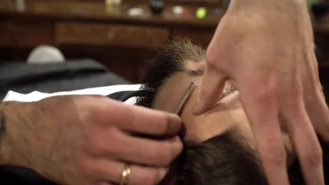 Concentrated Barber shaving beard of client with barber razor Stock Footage 69990055
