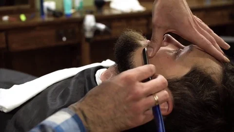 Concentrated Barber shaving beard of client with barber razor Stock Footage 69990118