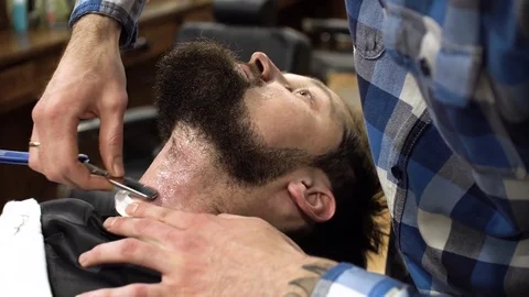Concentrated Barber shaving beard of client with barber razor Stock Footage 69990173