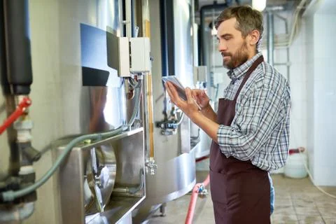 Concentrated beer engineer using tablet while examining equipment Stock Photos
