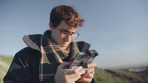 A concentrated boy flying a drone with the remote control connected to phone. Stock Footage 240397693