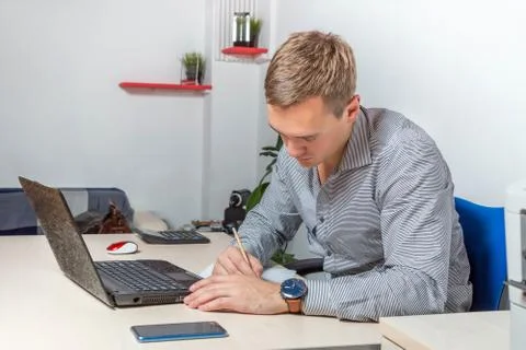 Concentrated businessman taking notes in front of the laptop and other equipm Foto stock