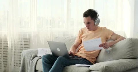 Concentrated caucasian man working with papers and laptop on sofa at home Stock Footage 246389250