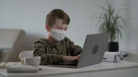 Concentrated child in mask doing homework using laptop typing  notes at home. 스톡 동영상 128396992