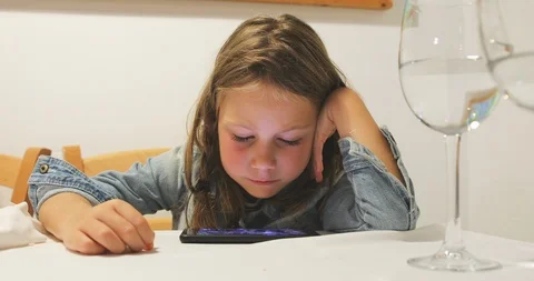 Concentrated child using smartphone sitting on chair of restaurant Stock Footage 118244820