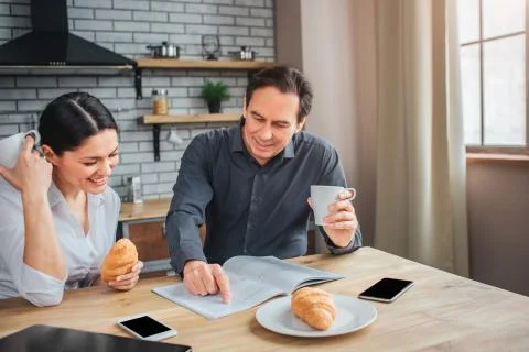 Concentrated couple sit at table in kitchen. Man point on journal page. Woman 写真素材