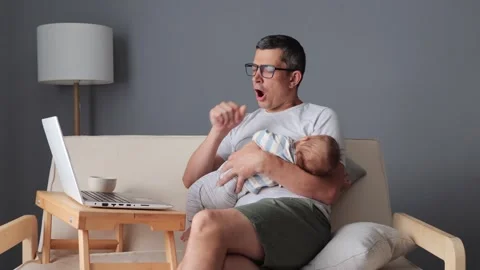 Concentrated dark-haired Caucasian man holding his son while using his laptop 動画素材 291290824