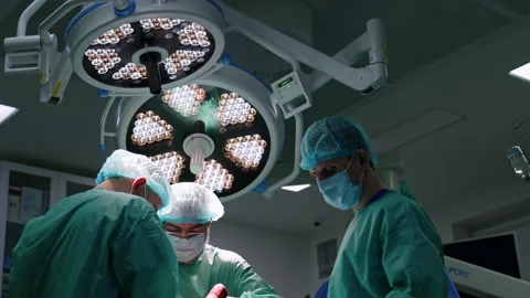 Concentrated doctors working under the round lamps in surgery room.  Stock Footage 252786837