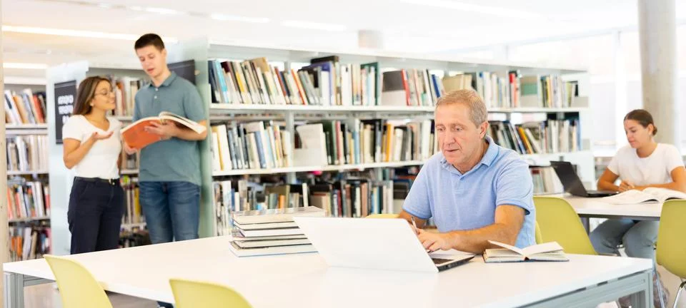 Concentrated elderly man checking planner while studying in the library and 스톡 사진