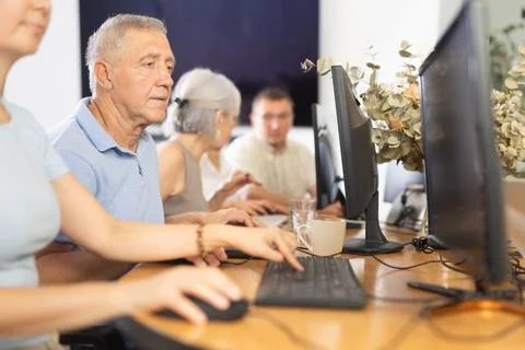 Concentrated elderly man immersed in using computer in library Fotos de archivo