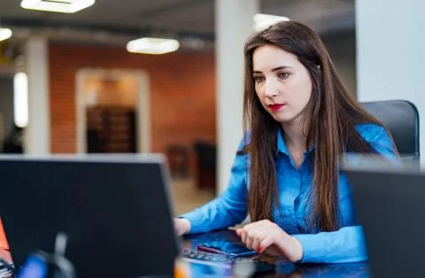 Concentrated female developer is working on a computer at modern office. Stock Photos