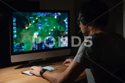 Concentrated Gamer In Headphones Using Computer For Playing Game