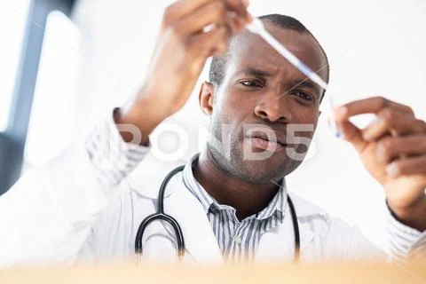 Concentrated international medical worker staring at test tube Stock Photos
