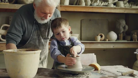 Concentrated little boy is learning to work with clay on throwing-wheel in Stock Footage 89377821