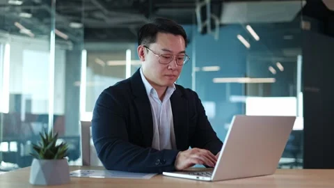 Concentrated man in glasses sitting in office and quickly typing text on laptop Video stock 271565166