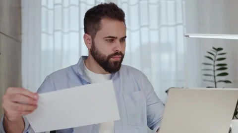 Concentrated man looking through documents in from of desktop with laptop Video stock 261946499