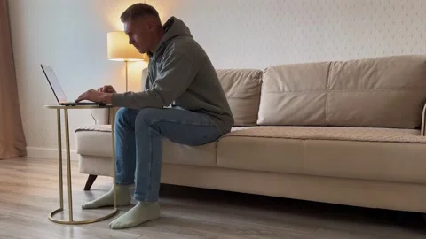 Concentrated man sitting on the couch using laptop for distance work from home. Stock Footage 317648272