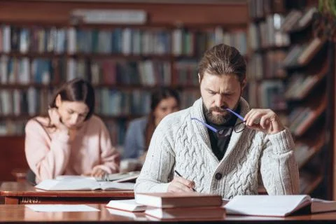 Concentrated man taking notes while reading books at library Stock Photos