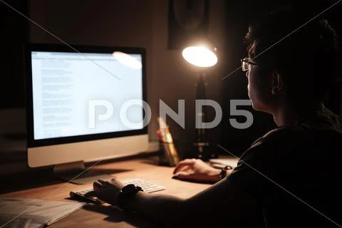 Concentrated man using computer sitting in dark room at home Stock Photos