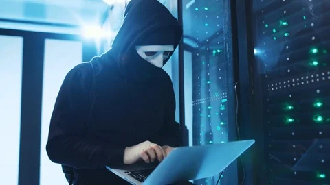 Concentrated masked hacker in hoodie coding malicious program on laptop, copying Stock Footage 120694814