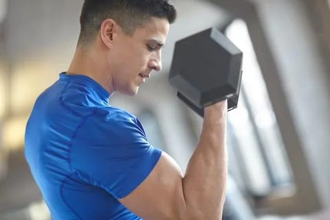 Concentrated power of will. a handsome young man lifting a dumbell in a gym. Stock Photos
