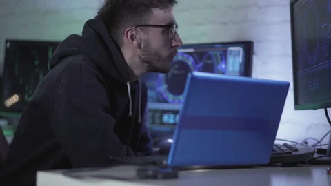 Concentrated programmer in eyeglasses working with multiple computers and laptop Stockbeeldmateriaal 141957514