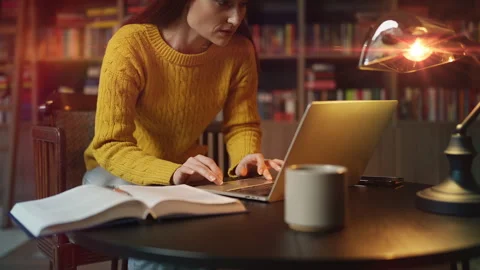 Concentrated red-haired woman working on laptop and researching in library Stock Footage 340267063
