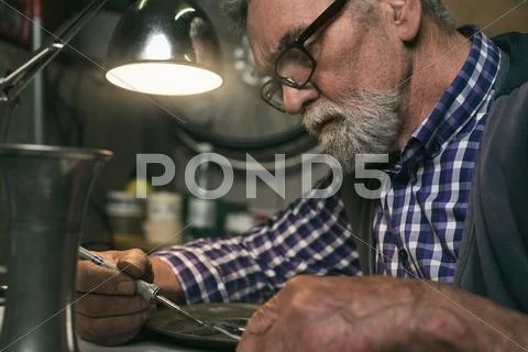 Concentrated senior man repairing tin plate in workshop. Stock Photos