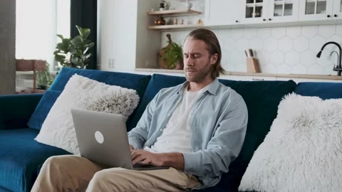 Concentrated seriously looking man is typing using his laptop sitting on a couch Video stock 236498502