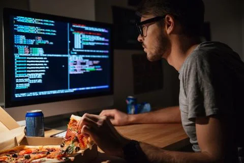 Concentrated software developer eating pizza and coding Foto stock