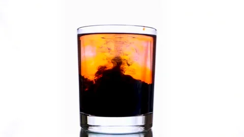 Concentrated stream of ink's being poured into a glass with orange colored water Video stock 159483605