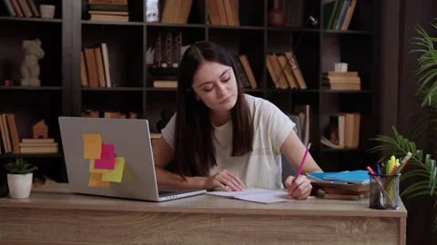 Concentrated student sitting at desk in library, writing essay, making notes in Stock Footage 304932080
