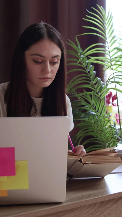 Concentrated student studies near window in library using laptop. Woman Stock Footage 305408161