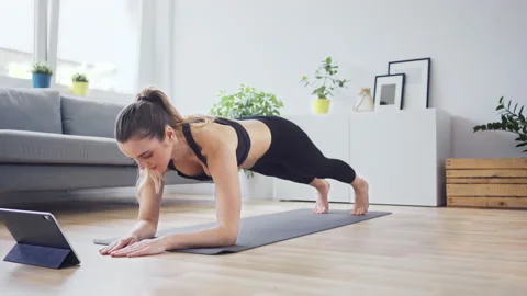Concentrated woman doing planks while watching online workout on digital tablet Stock Footage 141615951