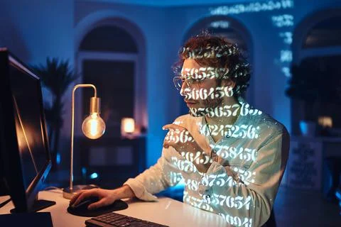 Concentrated on work caucasian guy using desk computer in dark room Stock Photos