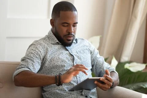 Concentrated young african american man holding digital tablet. Stock Photos