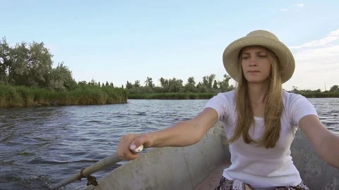 Concentrated young female rower using paddles to sail rusty old boat on calm Stock-Footage 95189198