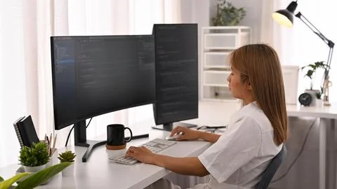 Concentrated young female software developer working with coded data in bright Foto stock
