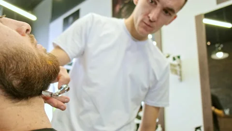 Concentrated young man holds scissors and trims man beard Stockbeeldmateriaal 142998419