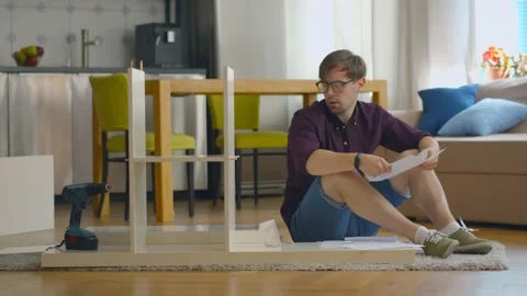 Concentrated young man reading instructions to assemble furniture in kitchen at Stock Footage 135669217