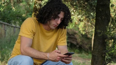 Concentrated young man typing on mobile phone and smiles reading a post 스톡 동영상 225478046