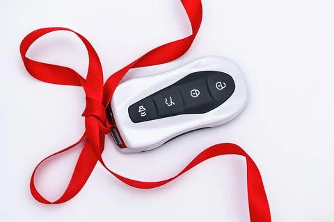 Concept and gift idea. Flat lay smart car key with a red gift ribbon on a whi Stock Photos