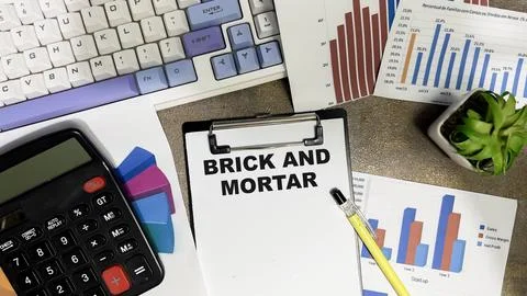 Concept of Brick and Mortar write on paperwork isolated on Wooden Table. Stock Photos